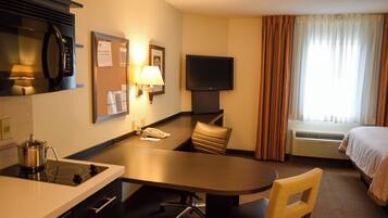 A hotel room with a kitchenette, a flat-screen TV, a bed, and a window with curtains.