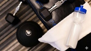 Une salle de sport avec des haltères, un kettlebell et une bouteille d’eau posée sur une serviette.