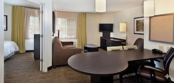Una habitación de hotel con cama, sofá, mesa de comedor, televisión y lámpara.