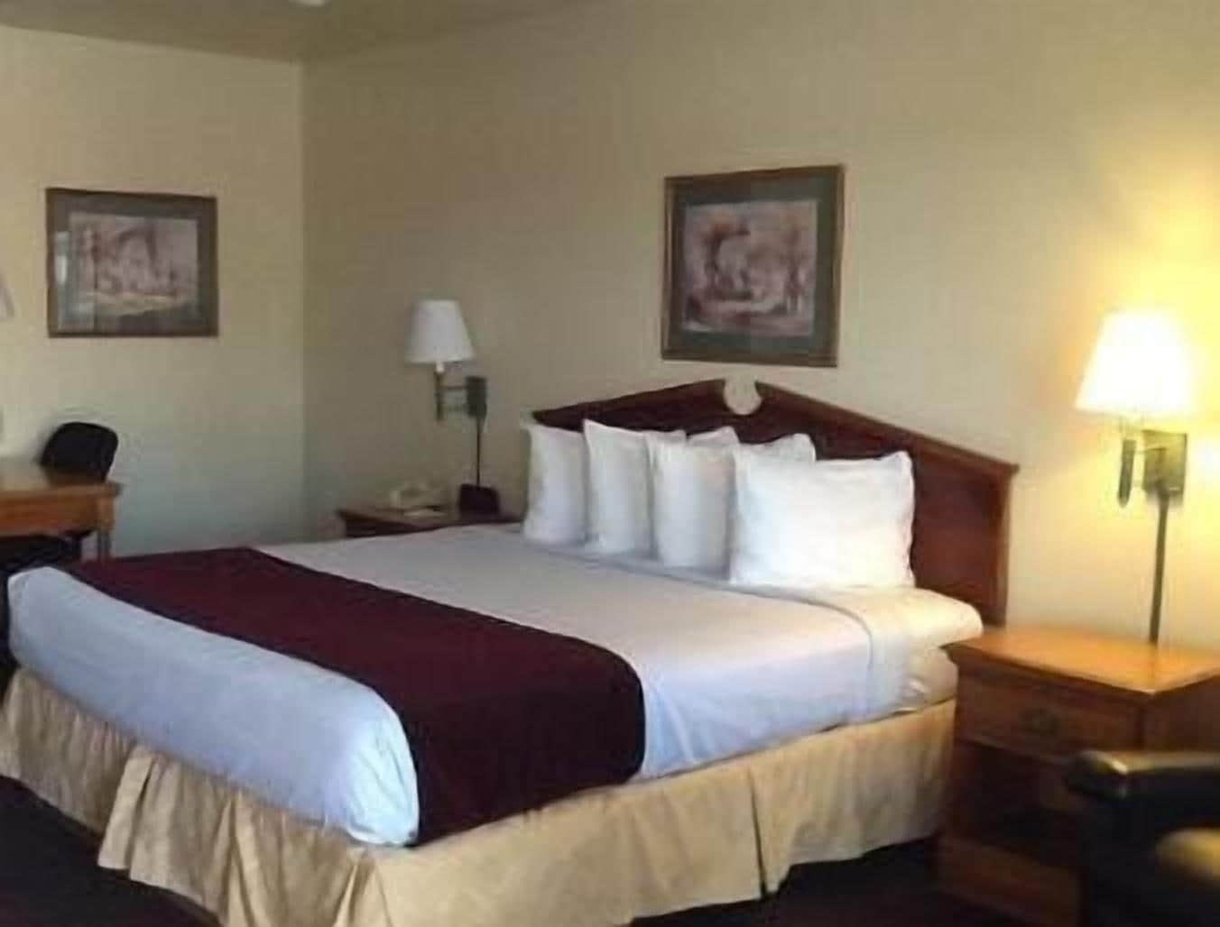 Una habitación de hotel con una cama grande, una mesita de noche, una lámpara y dos cuadros en la pared.