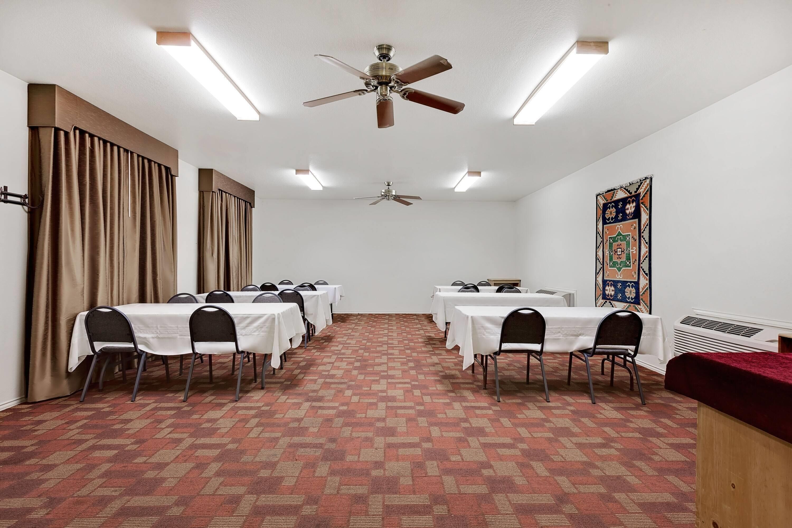 Un salón de conferencias con mesas, sillas, ventiladores de techo y una alfombra estampada.