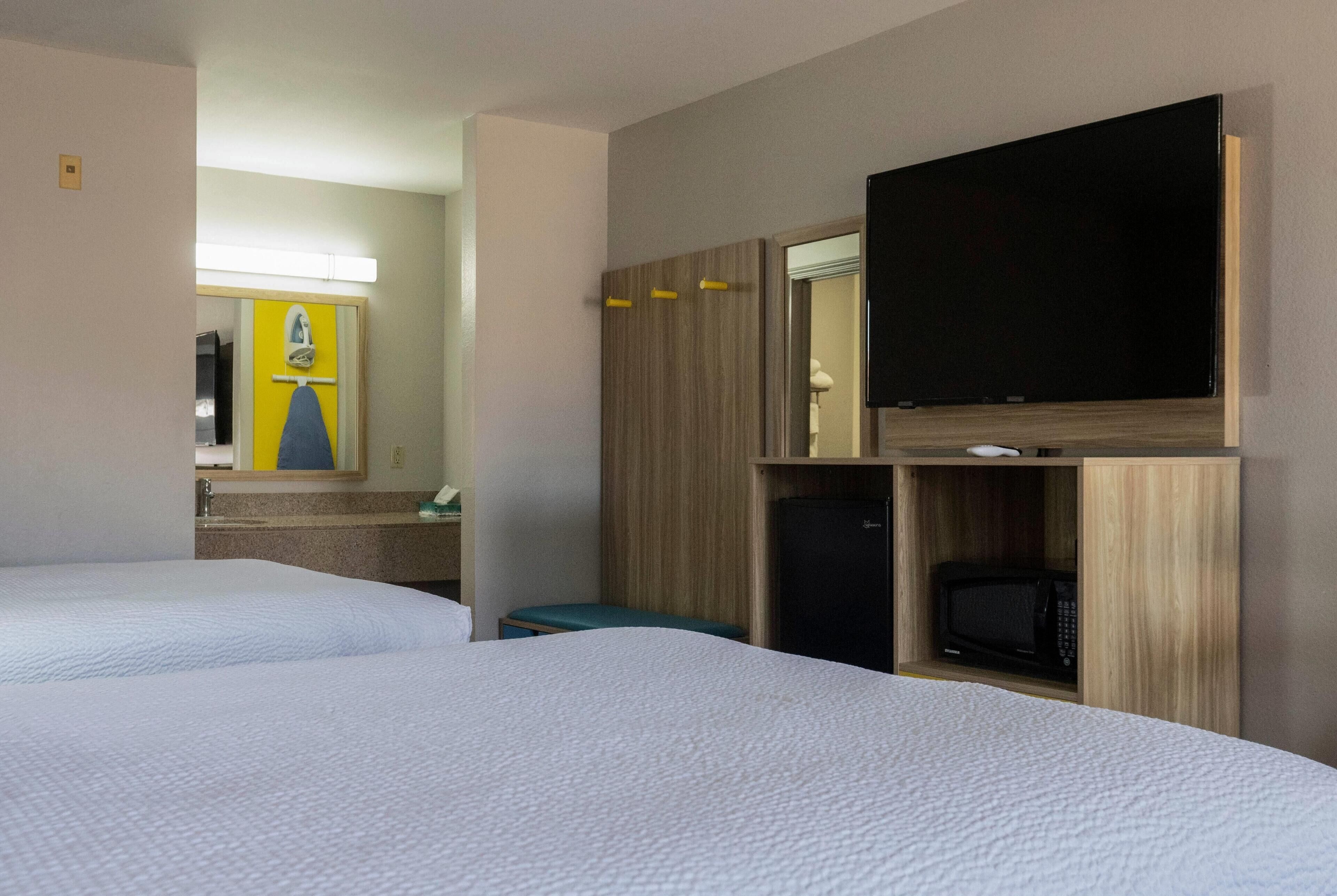 Een hotelkamer met twee bedden, een televisie, een magnetron en een spiegel.