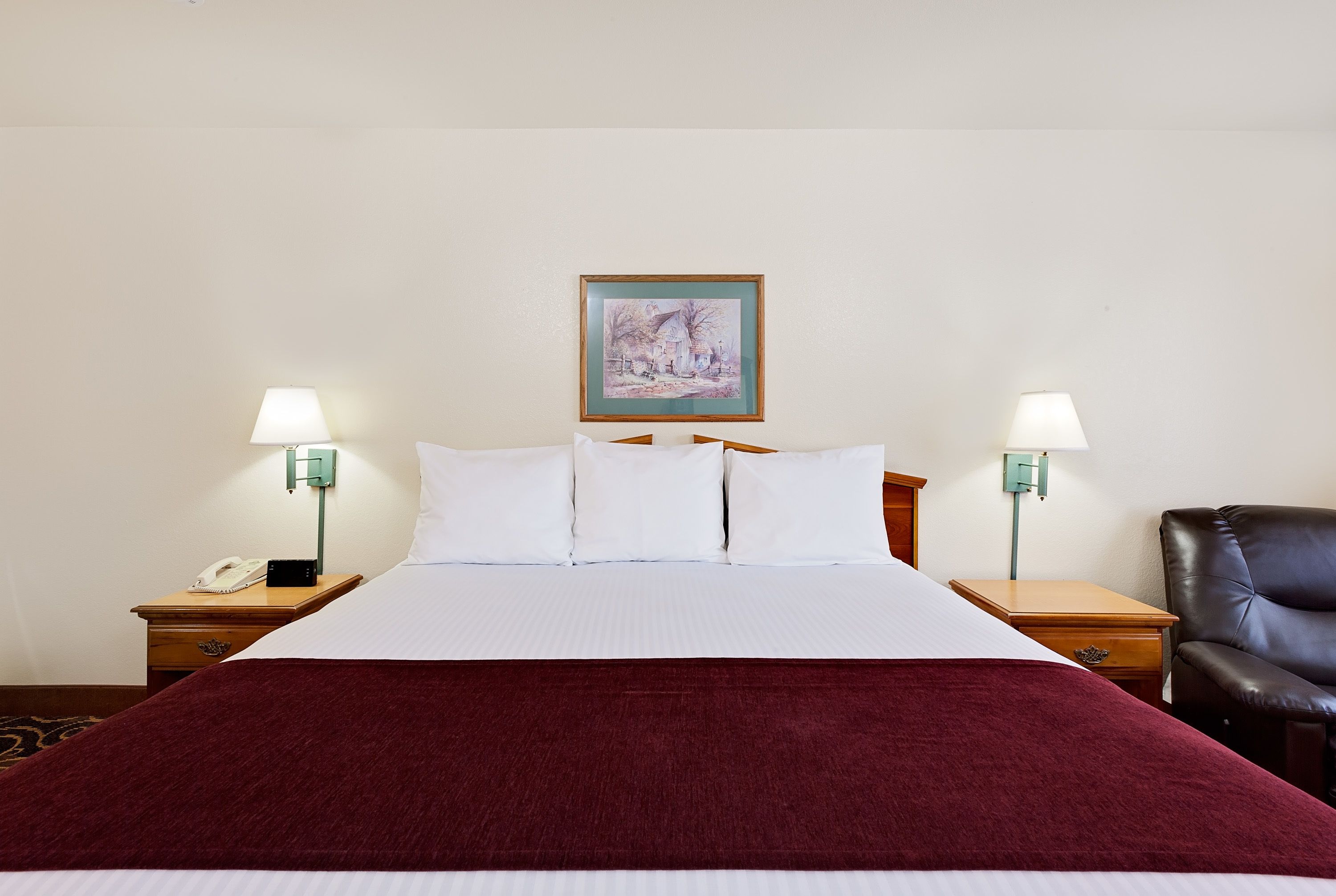 Habitación de hotel con una cama grande, dos mesitas de noche con lámparas, una silla y un cuadro en la pared.