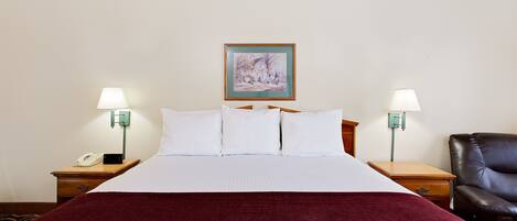 Habitación de hotel con una cama grande, dos mesitas de noche con lámparas, una silla y un cuadro en la pared.