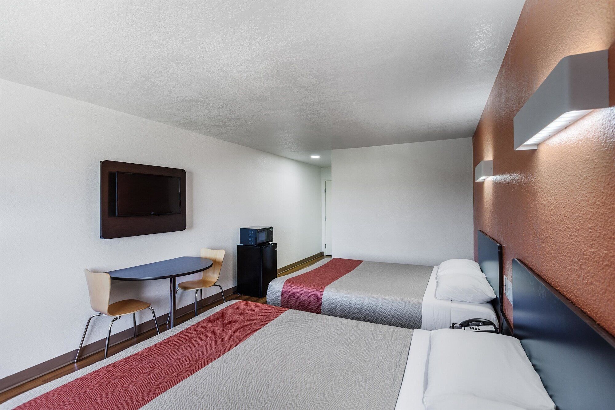 A hotel room with two beds, a desk, a chair, a TV, and a microwave.