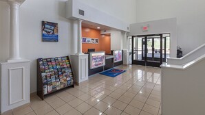 A hotel lobby with a reception desk, a bulletin board with magazines, and a staircase leading to another floor. - Motel 6 Bedford, TX - Fort Worth (Bedford)