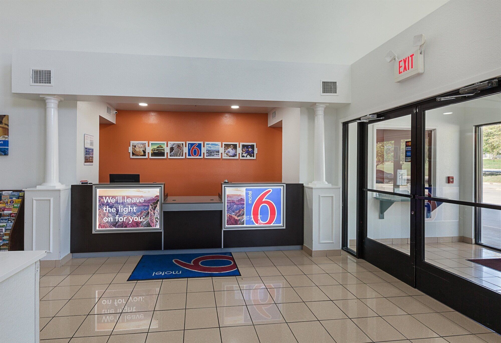 A hotel reception area with a reception desk, a digital screen displaying a message, a number 6 sign, and an exit sign.