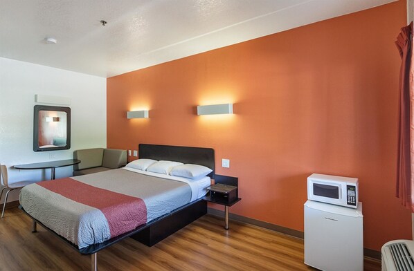A hotel room with a bed, bedside table, chair, and a microwave.