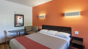 A hotel room with a bed, a desk, a chair, and two wall-mounted lights. - Motel 6 Bedford, TX - Fort Worth (Bedford)