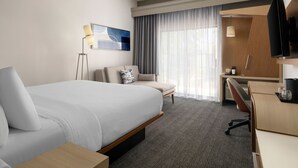 Een hotelkamer met een groot bed, een bureau, een stoel, een televisie en een raam met gordijnen.