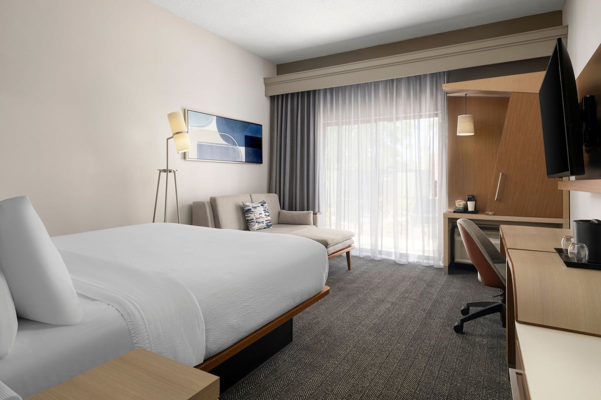 Een hotelkamer met een groot bed, een bureau, een stoel, een televisie en een raam met gordijnen.