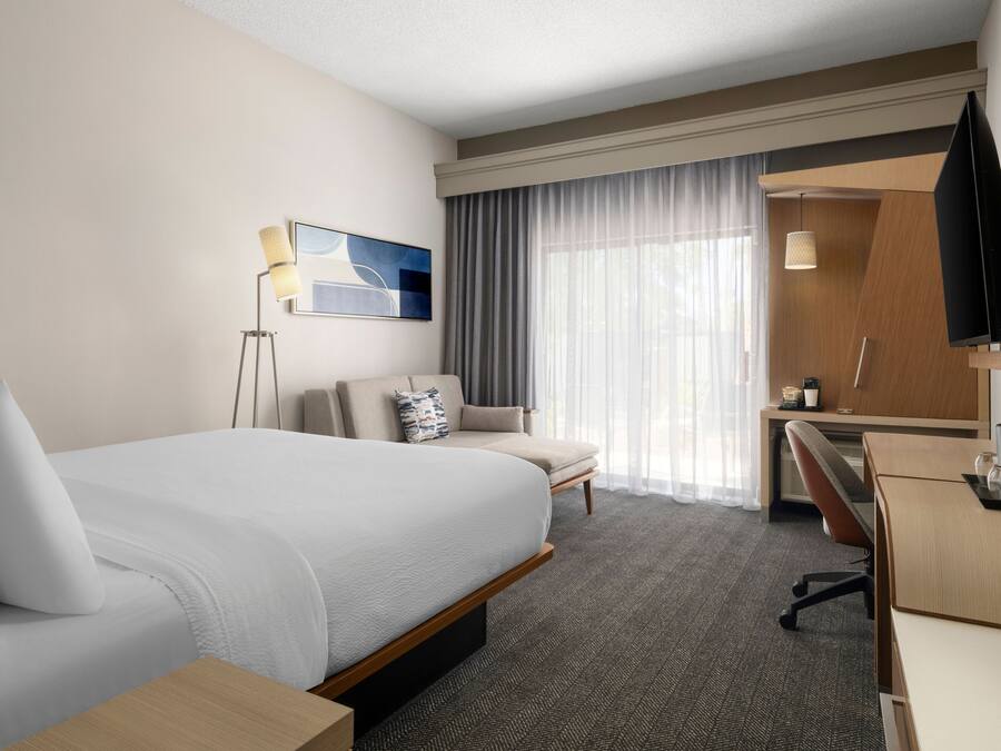 Una habitación de hotel con una cama grande, un escritorio, una silla, un televisor y una ventana con cortinas.