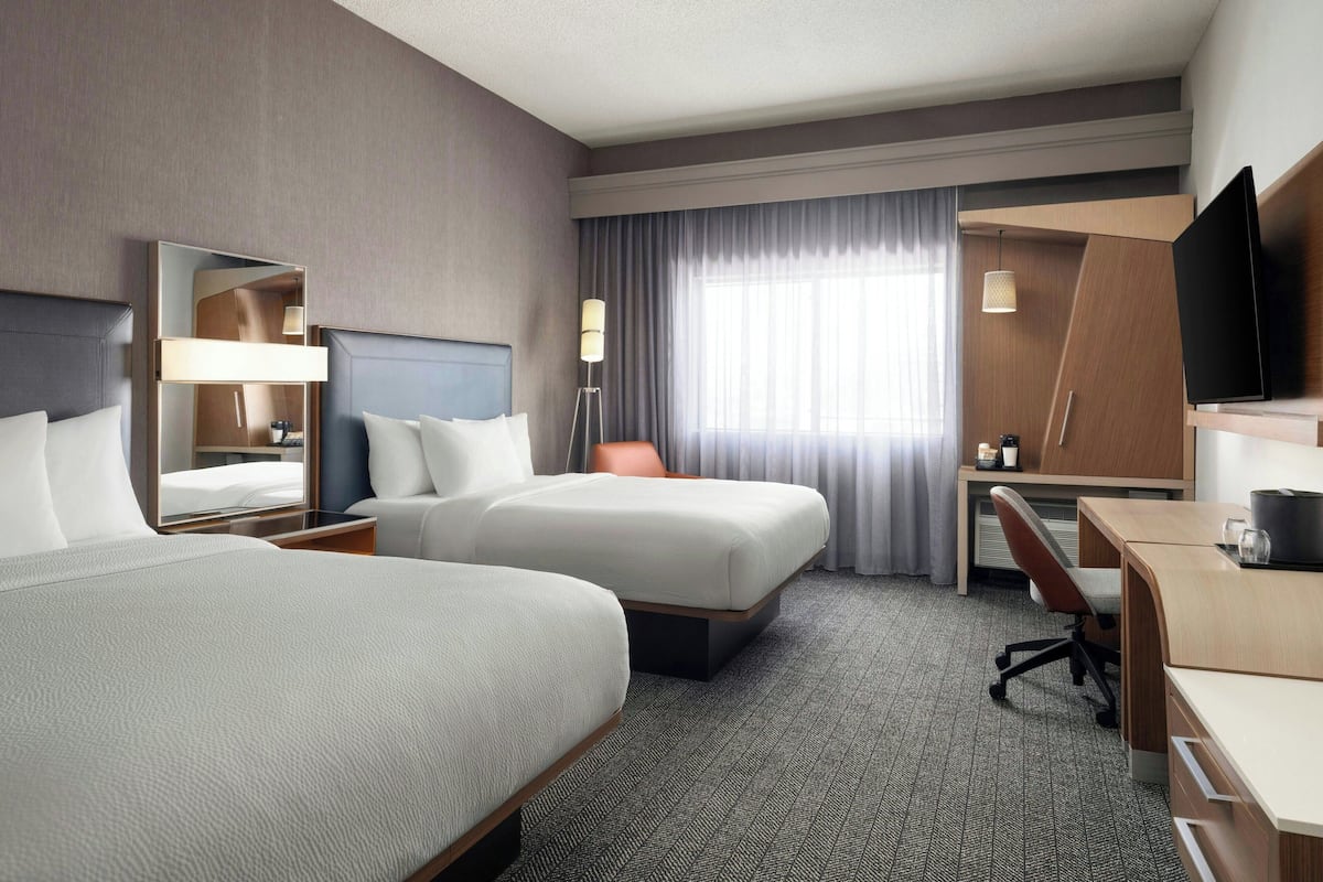 Hotelkamer met twee bedden, een bureau, een stoel, een televisie en een groot raam met gordijnen.