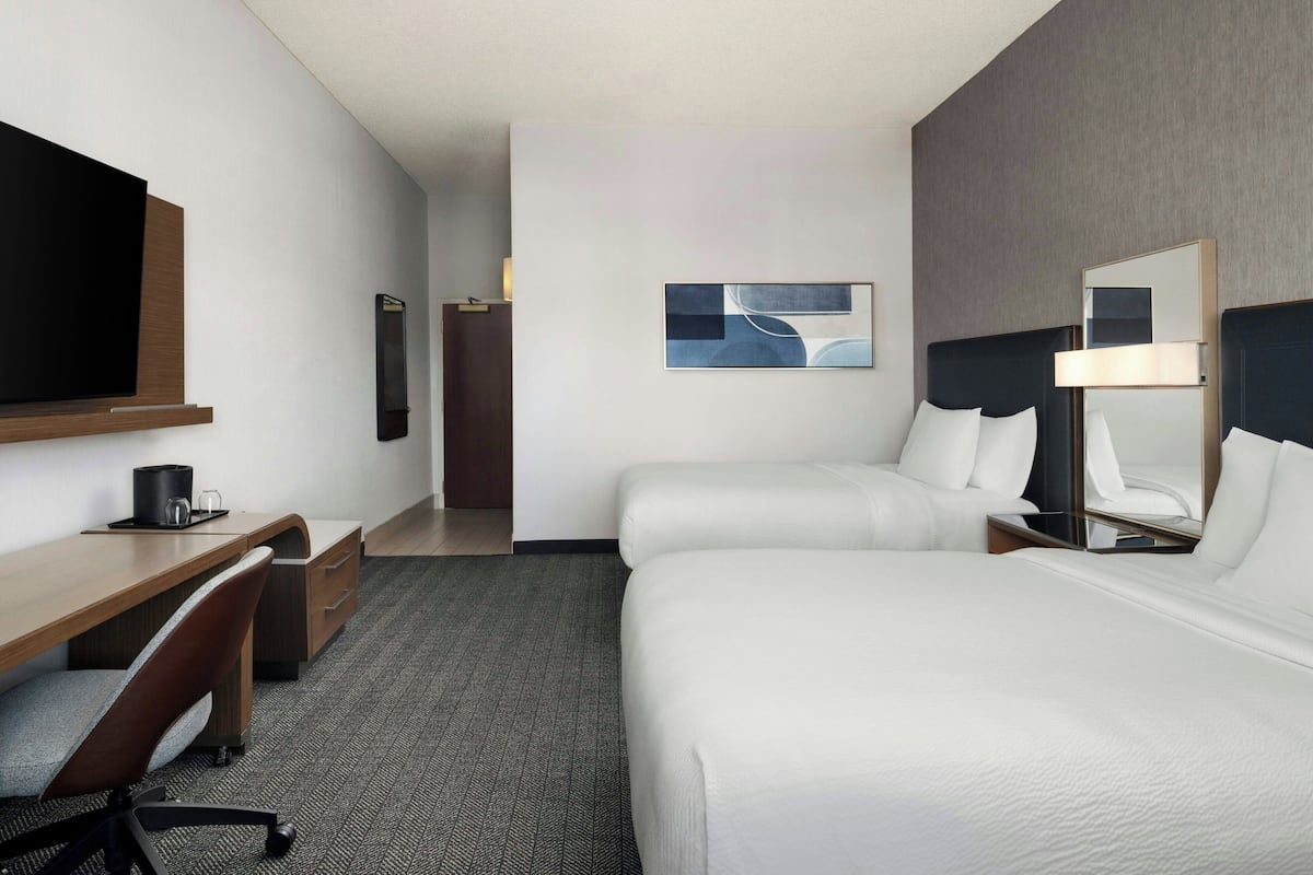 Een hotelkamer met een bed, een bureau, een stoel, een televisie, een spiegel en een schilderij aan de muur.