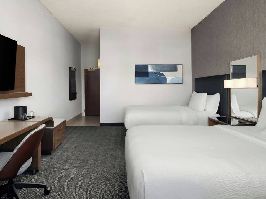 Een hotelkamer met een bed, een bureau, een stoel, een televisie, een spiegel en een schilderij aan de muur.