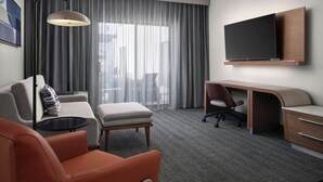 Een moderne hotelkamer met een bank, voetenbankje, bureau, stoel en een flatscreen televisie aan de muur.