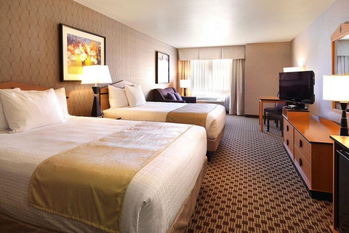 A hotel room with two beds, a desk with a television, and a large window with curtains.