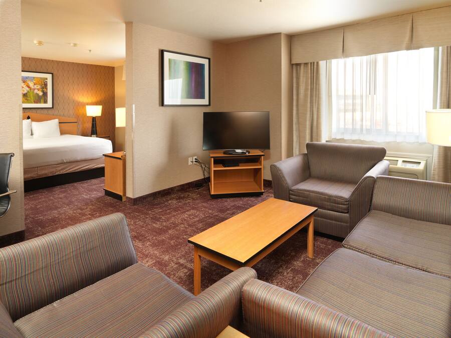 Quarto de hotel com cama, televisão, sofá, mesa de centro e piso coberto por carpete.