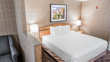 Habitación de hotel con una cama grande, dos lámparas de noche, cabecera, un cuadro en la pared y una silla.
