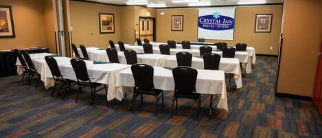 A conference room with multiple tables and chairs, a carpeted floor, and a banner for Crystal Inn Hotel Suites.