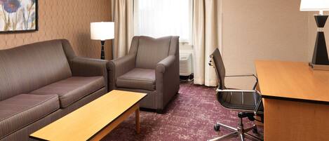 A hotel room with a sofa, armchair, desk, and a lamp.