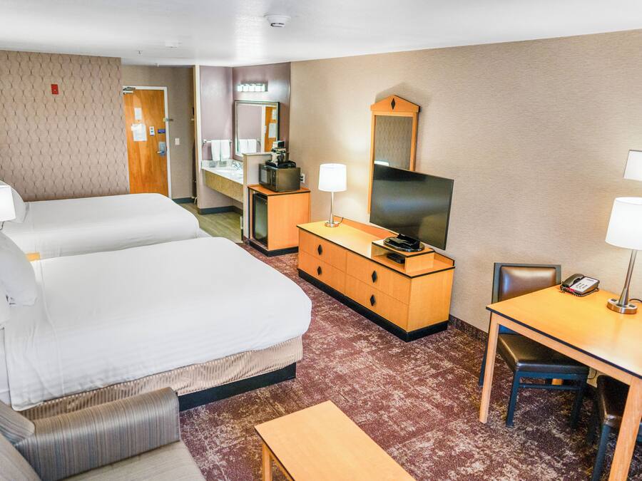 A hotel room with two beds, a desk with a chair, a television, and a small table.