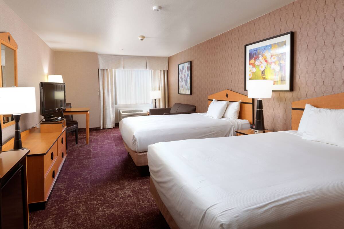 A hotel room with two beds, a desk, a television, and a window with curtains.