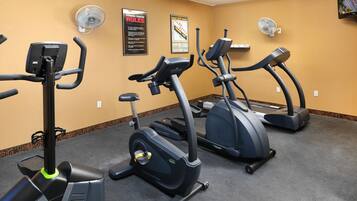 A fitness center with multiple treadmills, wall-mounted fans, and a posted rules sign.