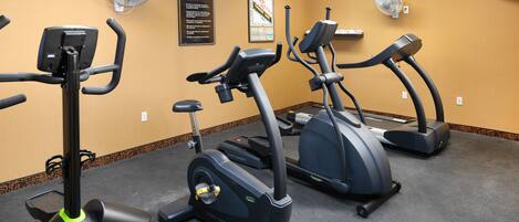 Un gimnasio con cintas de correr, ventiladores en la pared y un cartel con las normas.