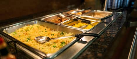A buffet with various dishes, including a large tray of pasta garnished with herbs.