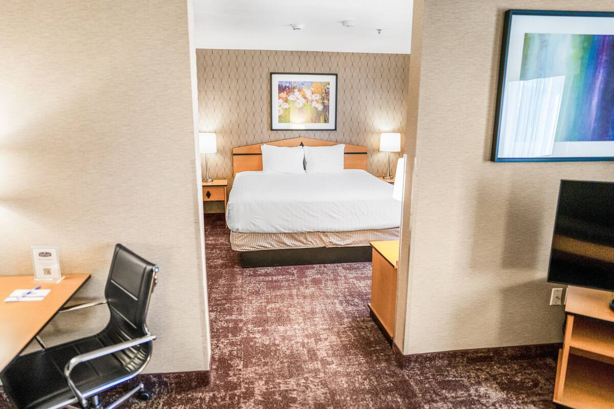 A hotel room with a bed, two bedside tables, a desk with a chair, a television, and a framed picture on the wall.