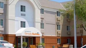 A hotel with a white and beige exterior, a 'Sonesta Simply Suites' sign, and a parking area with cars and benches. - Sonesta Simply Suites Phoenix Glendale (Phoenix)