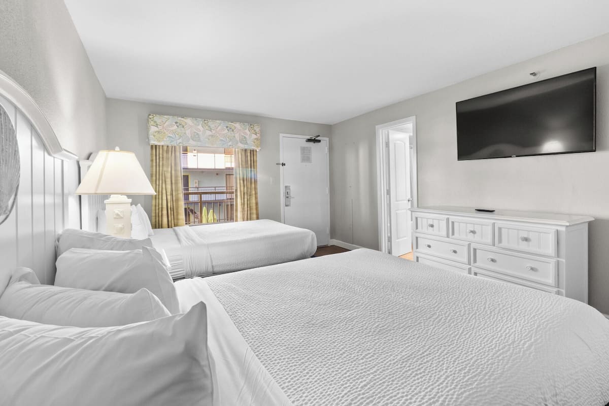 A hotel room with two beds, a TV, a dresser, and a window with curtains.
