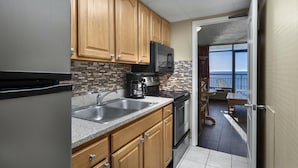 A kitchen with wooden cabinets, a stainless steel refrigerator, a microwave, and a coffee maker. There is a view of a balcony with a table and chairs.
