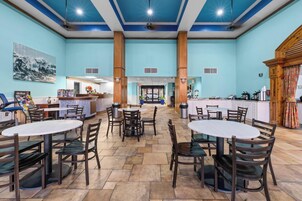 A spacious indoor area with multiple round tables and chairs, a reception desk, and a kitchen area.