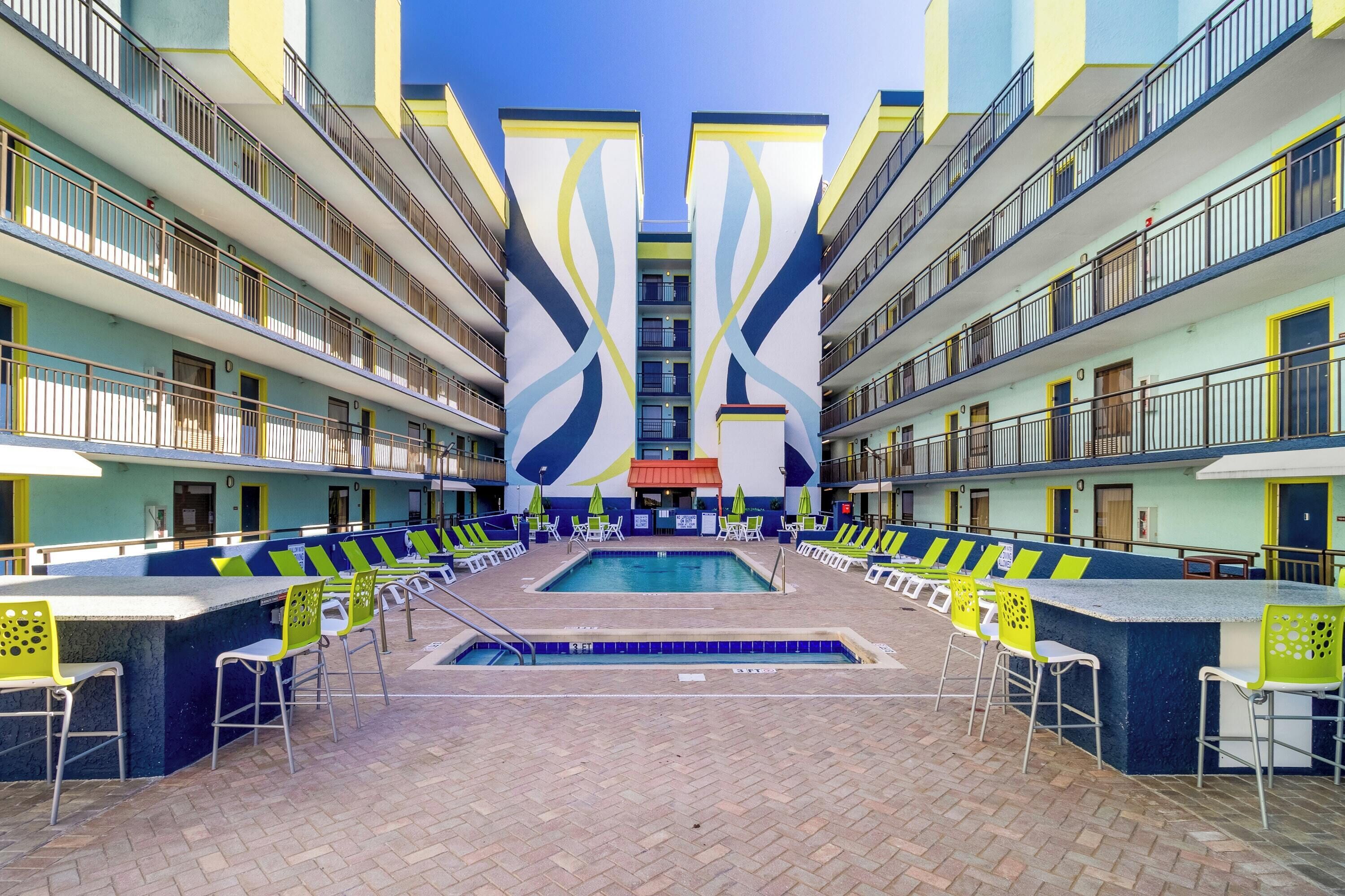 Un vestíbulo de hotel con piscina central, varios balcones y zonas de estar al aire libre.
