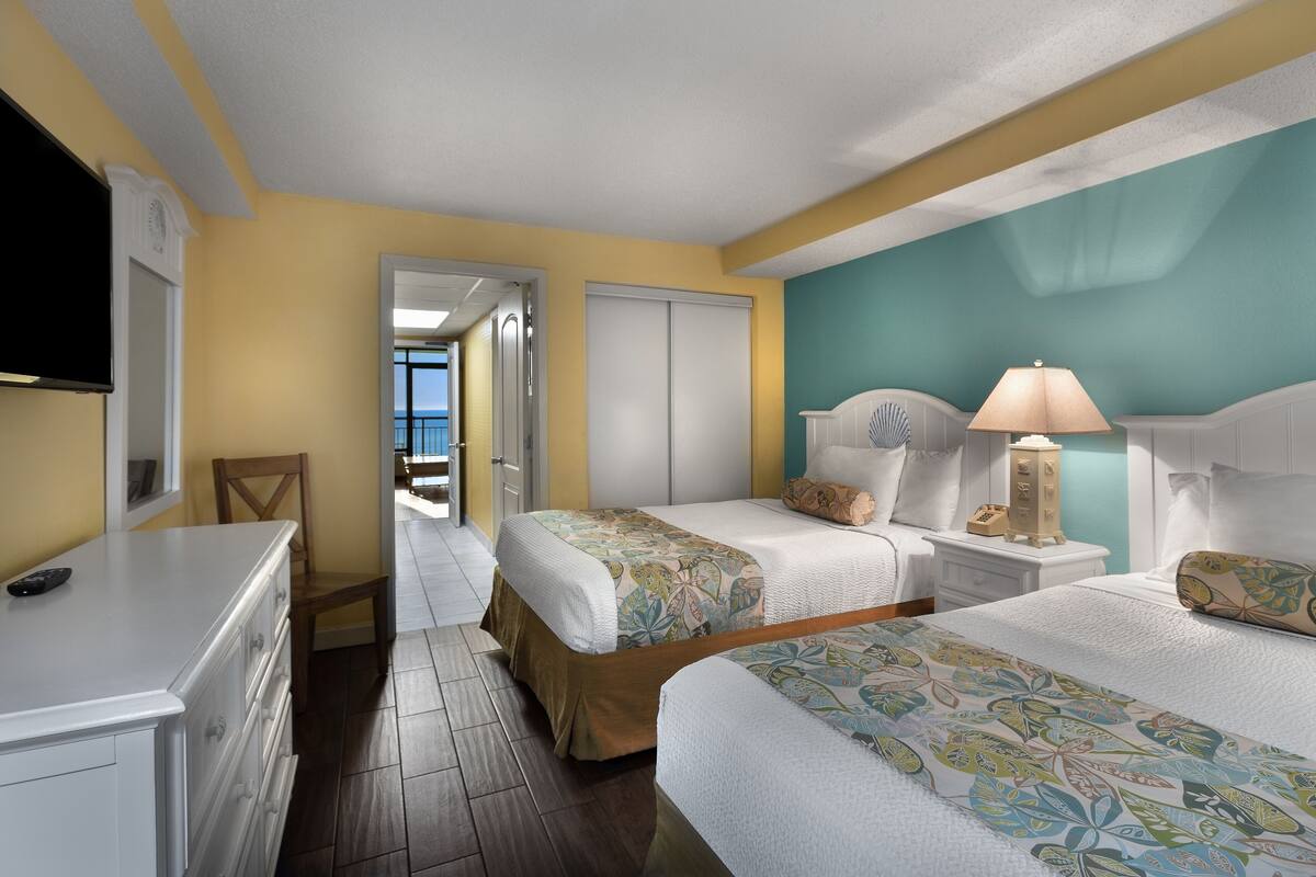 A hotel room with two beds, a nightstand with a lamp, a dresser, and a television.