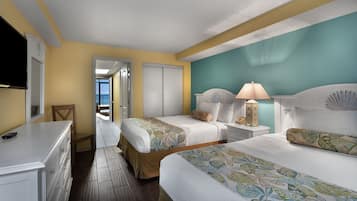 A hotel room with two beds, a nightstand with a lamp, a dresser, and a television.