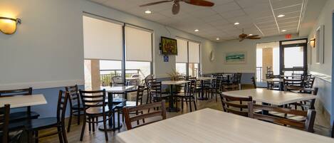 A restaurant with multiple tables and chairs, ceiling fans, and large windows.