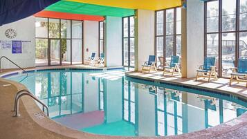 An indoor swimming pool with clear water, surrounded by lounge chairs and a covered area with a colorful roof.