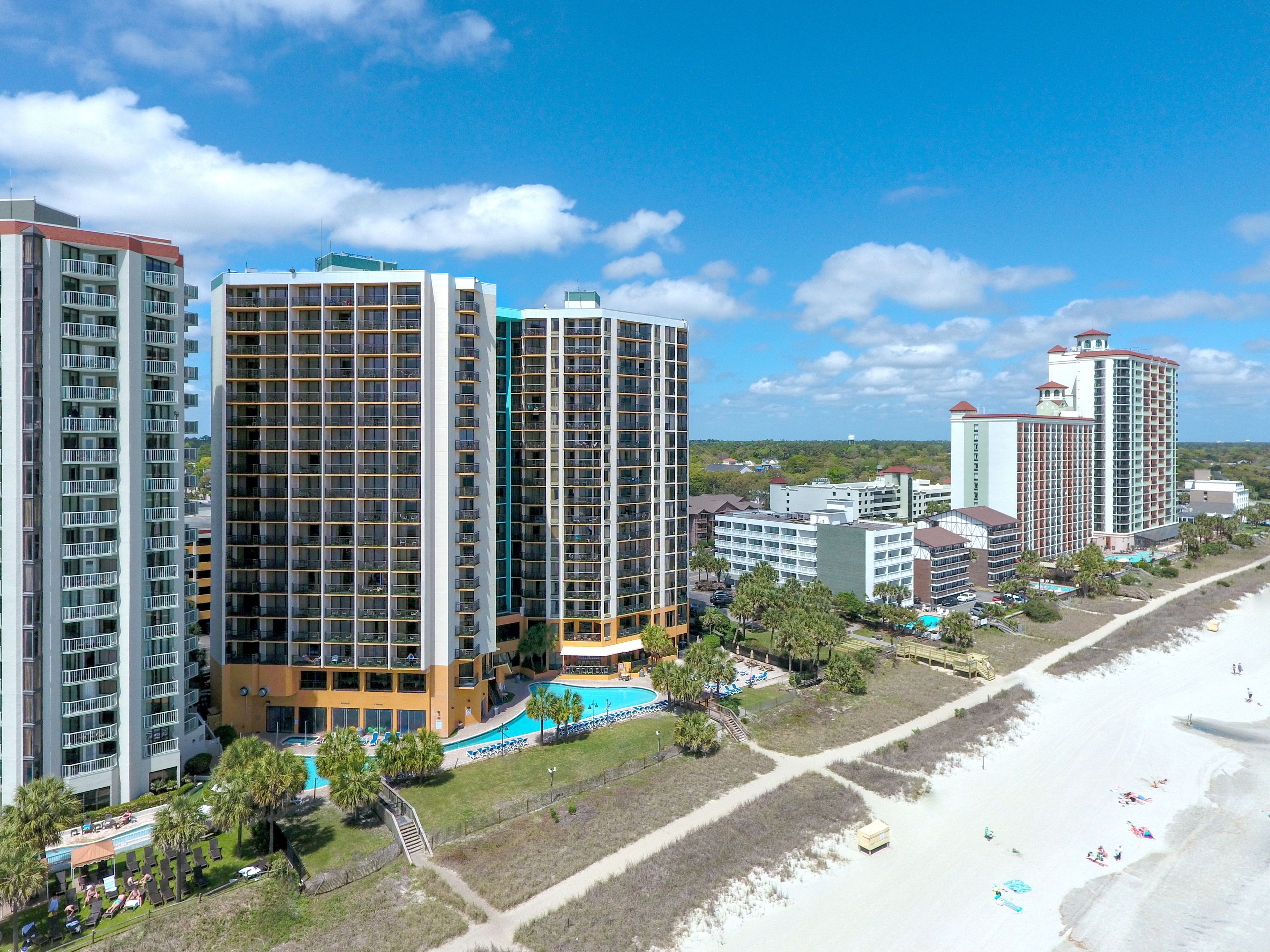 A high-rise hotel with multiple balconies, a swimming pool, and a beach view.
