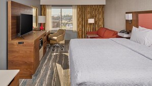 A hotel room with a bed, a desk with a TV, a chair, a desk lamp, a telephone, and a window with curtains. - Hampton Inn Anchorage (Anchorage)