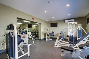 A gym with various exercise machines, a television mounted on the wall, and a door leading to another room. - Holiday Inn Express Fort Campbell-Oak Grove by IHG (Oak Grove)