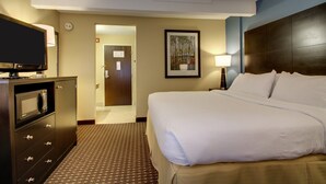 Quarto de hotel com cama, televisão, cômoda e um quadro na parede.