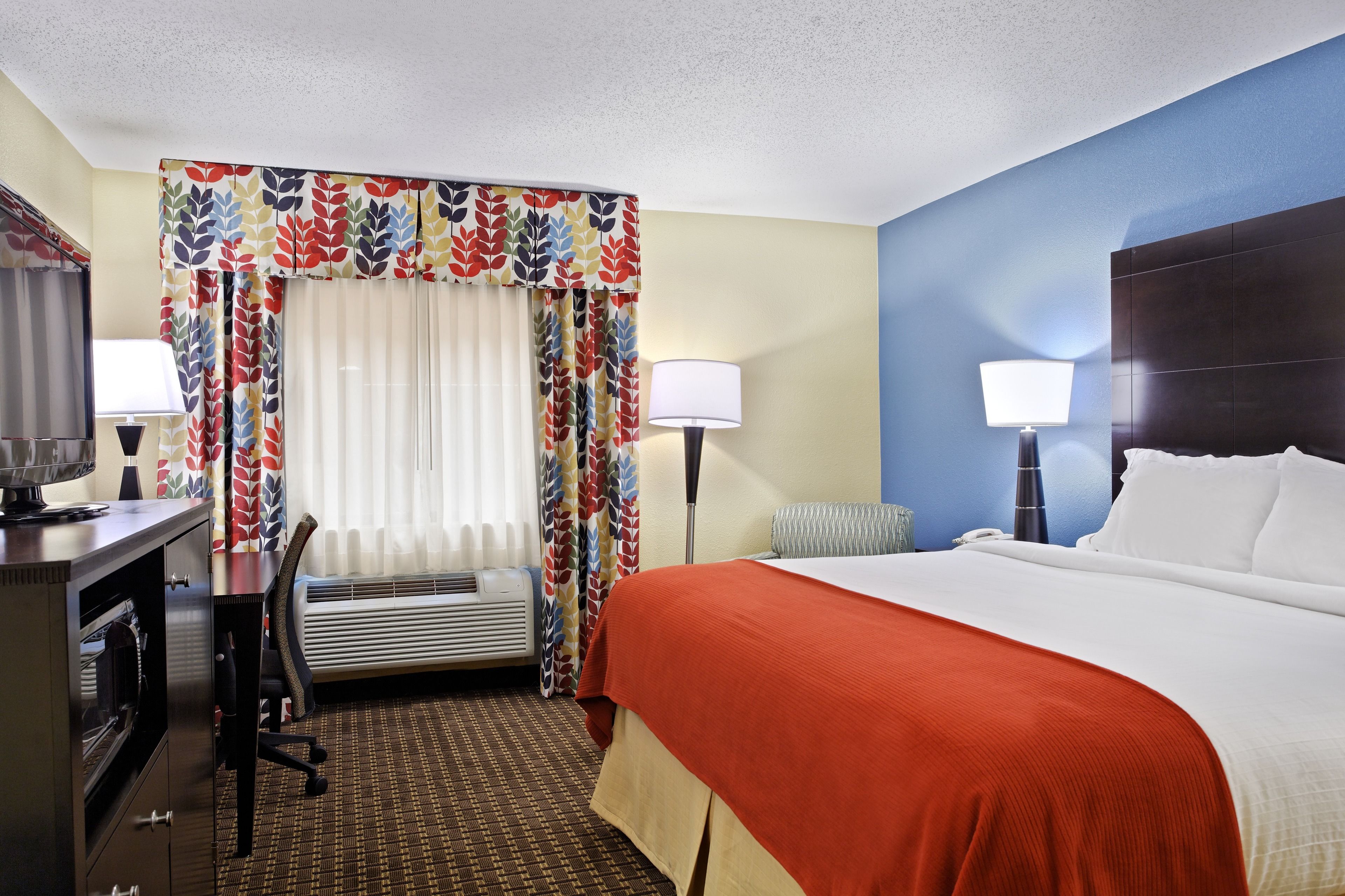 Quarto de hotel com cama, escrivaninha, cadeira e luminárias.