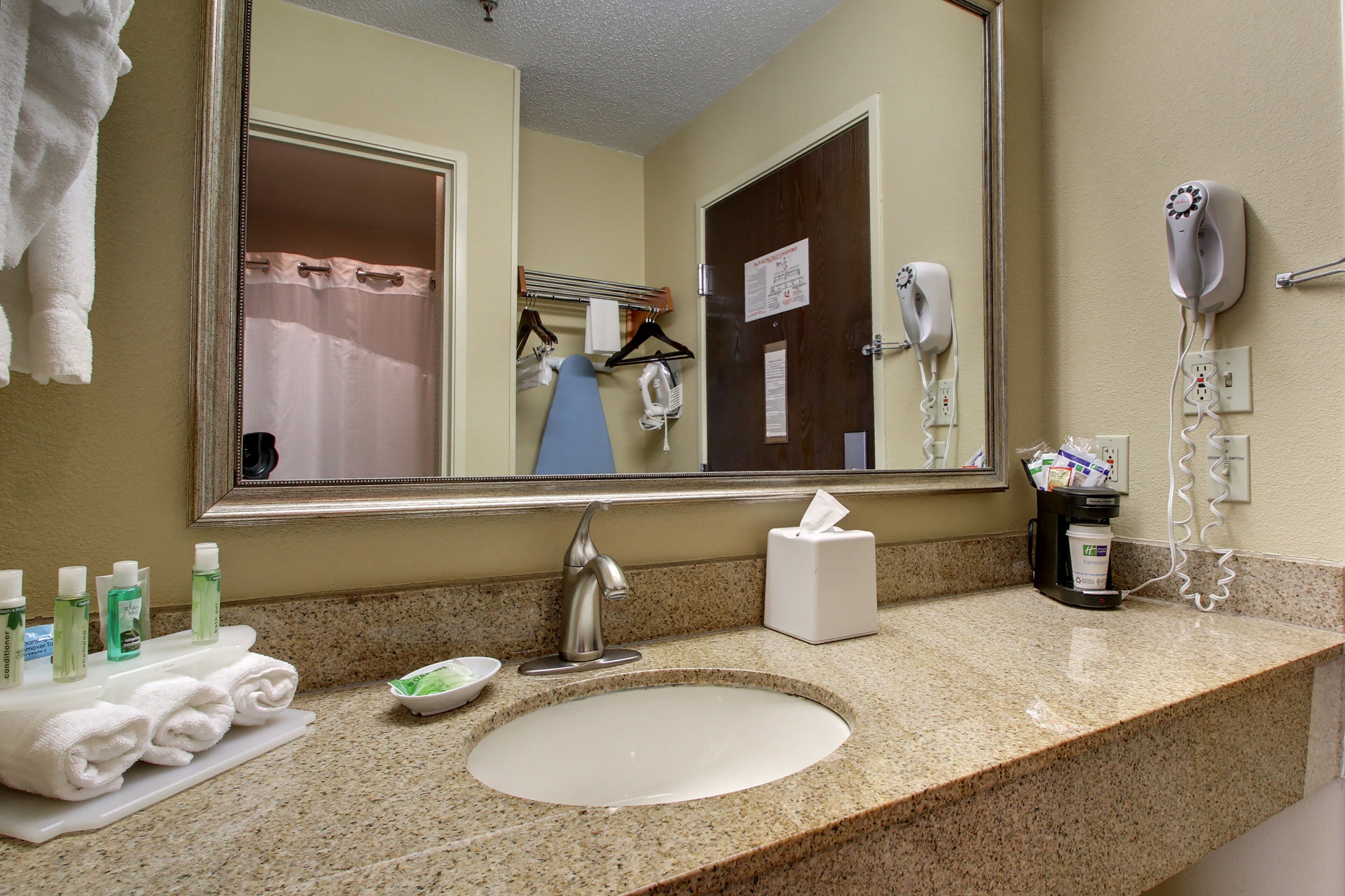 A hotel bathroom with a sink, mirror, towel rack, hairdryer, and toiletries.