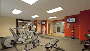 A gym with various exercise machines, a wall clock, and a television screen.