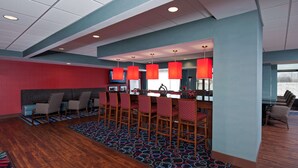 A modern hotel lobby with a red seating area, a bar with red pendant lights, and a patterned carpet.