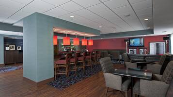 A hotel lobby with a bar area, seating, and a television screen.