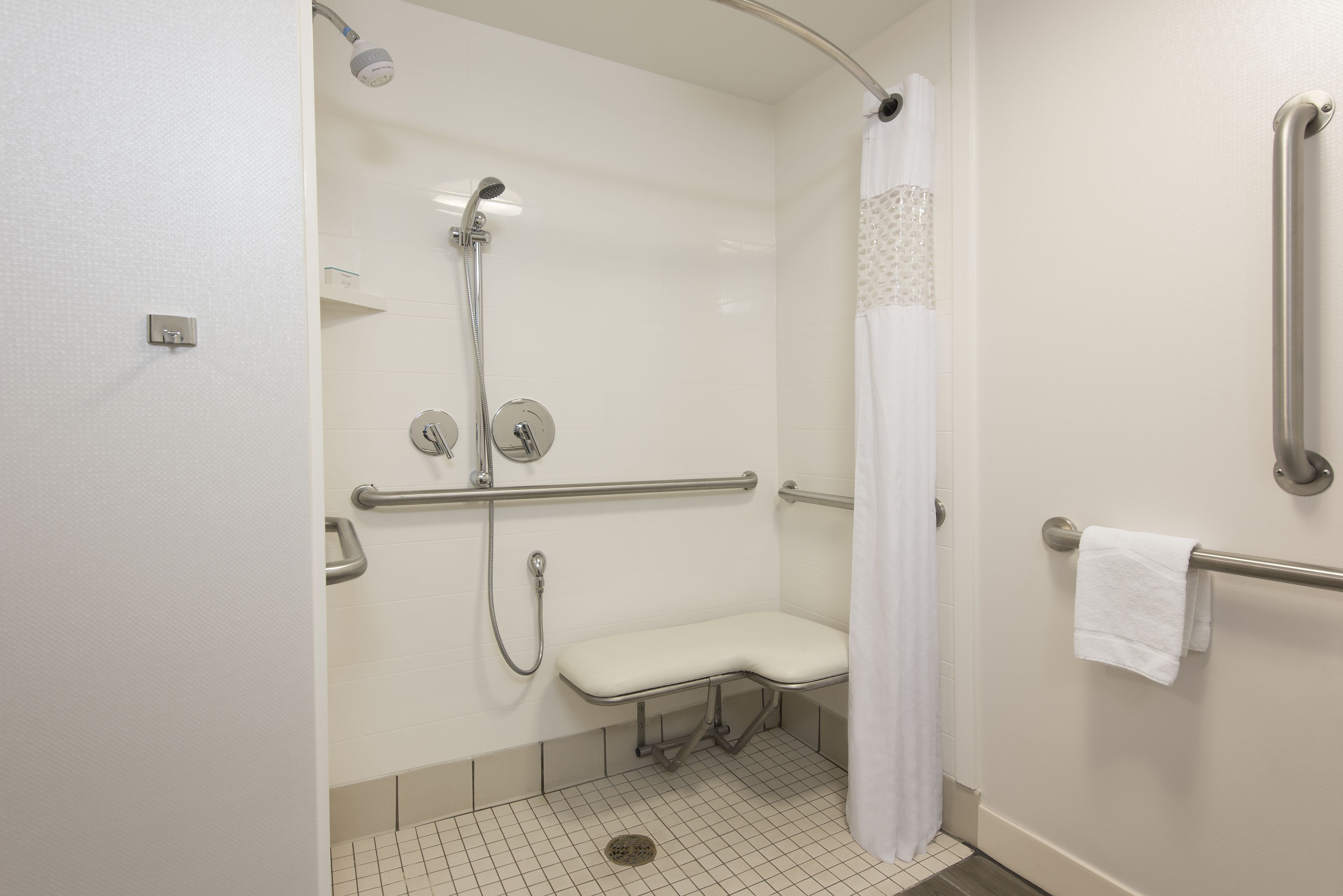 A handicap-accessible shower with a bench, grab bars, and a white curtain.